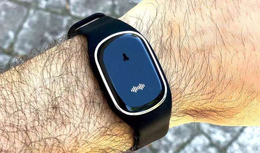 The image shows a bracelet worn on the wrist, called Moskitopro. It is black in color with a minimalist and smooth screen, featuring a small icon and a sound wave at the bottom. The bracelet is intended to protect against mosquito bites by emitting ultrasonic waves.